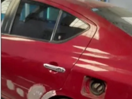 Nissan Versa rojo con el panel lateral trasero masillado antes de pintar