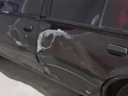 Lateral de un sedán granate con la puerta hundida y la pintura saltada tras un golpe